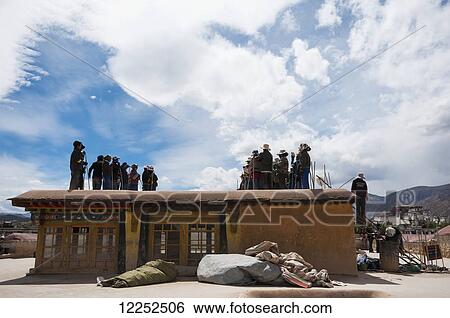 Stock Photograph - Workers dancing and singing while repairing the roof of Jokhang Temple, Potala Palace in the distance; Lhasa, Tibet, China. Fotosearch