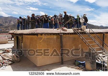 Stock Photography - Workers dancing and singing while repairing the roof of Jokhang Temple, Potala Palace in the distance; Lhasa, Tibet, China. Fotosearch