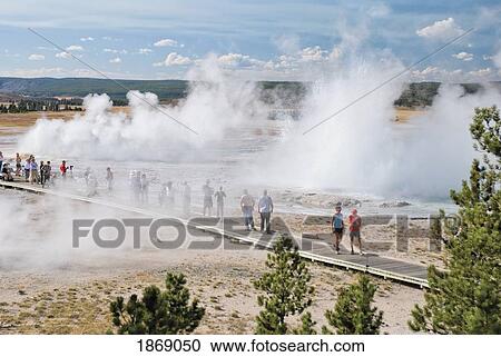 Stock Image - Yellowstone National Park, United States Of America; A Crowd Watches Erupting Geysers At The Upper Geyser Basin. Fotosearch