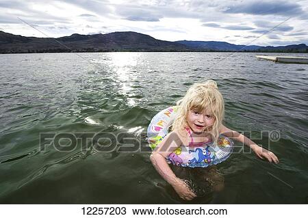 Stock Image - Young blonde girl floating in a lifebuoy; Osoyoos, British Columbia, Canada. Fotosearch