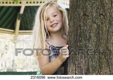Young Blonde Girl Smiling And Looking Out From Behind A Tree; Ontario Canada View Large Photo Image Stock Photograph - Young Blonde Girl Smiling And Looking Out From Behind A Tree; Ontario Canada. Fotosearch