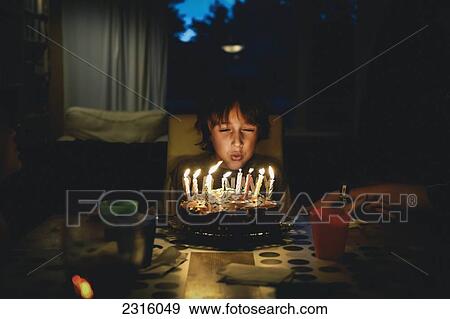 Stock Photo - Young Boy Blowing Candles On Birthday Cake In The Dark; Otterburn Park Quebec Canada. Fotosearch