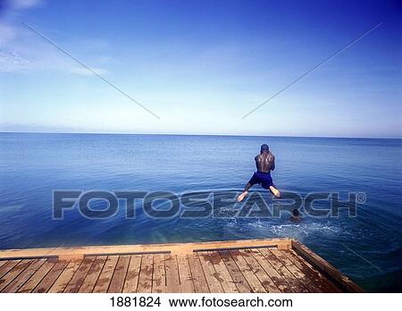 Picture - Young Boy Jumping Off Pier Into Waters Of Grand Anse Beach. Fotosearch
