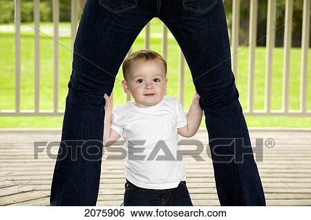 Stock Photograph - Young Boy Looking Out From His Mother's Legs; Ontario Canada. Fotosearch