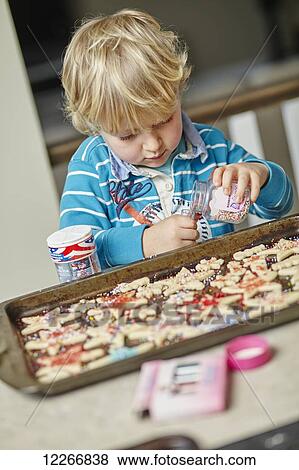 Stock Photo - Young boy pouring sprinkles for homemade cookies; Ontario, Canada. Fotosearch