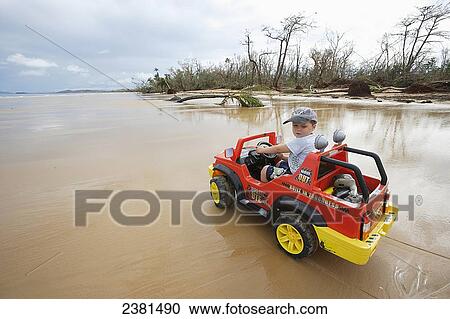 Stock Image - Young boy rides his toy battery operated car along the beach near Tully after cyclone Yasi had just battered the coast; Queensland, Australia. Fotosearch