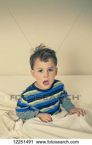 Stock Image - Young boy sitting in bed complaining; Connecticut, United States of America. Fotosearch