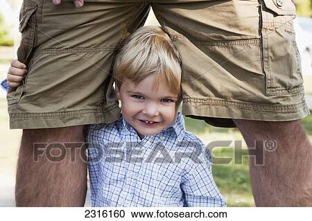 Stock Image - Young Boy Smiling And Hugging His Dad's Legs; Ontario Canada. Fotosearch