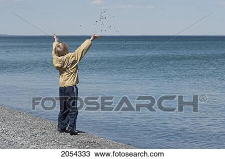 Stock Image - Young Boy Throwing Rocks Into Lake Ontario, Picton, Ontario. Fotosearch