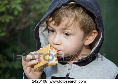 Stock Photo - Young boy trying to eat a sticky s'more outdoors; Edmonton, Alberta, Canada. Fotosearch