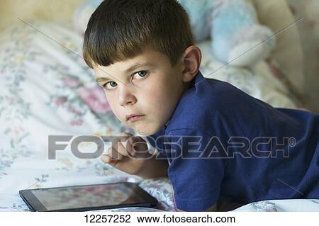 Stock Image - Young boy using a computer tablet on a bed; Lemington, Newcastle Upon Tyne, England. Fotosearch