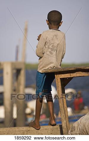 Stock Image - Young Boy Watching The Boats Come And Go, Lamu, Kenya, East Africa. Fotosearch