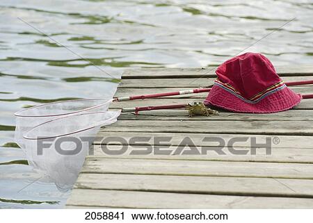 Stock Image - Young Boy's Sunhat, Frog Nets And Bull Frog Sitting On Dock Over Looking Small Lake, South Eastern Ontario. Fotosearch