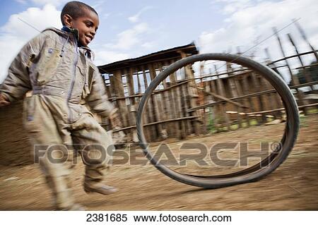 Stock Photography - Young child rolling a tire down a dirt road; Debarq, Simien mountains, Ethiopia. Fotosearch