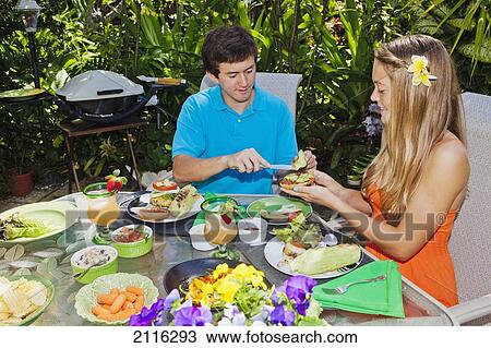 Stock Image - Young couple at an oudoor barbeque lunch in a Hawaiian garden.. Fotosearch