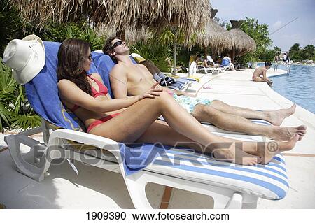 Stock Image - Young Couple Sunbathing By Swimming Pool, Mayan Riviera, Yucatan Peninsular, Quintana Roo State, Mexico. Fotosearch