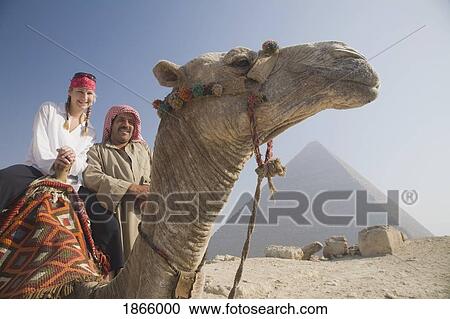 Stock Image - Young Female Tourist On A Camel With A Local Guide At The Pyramids Of Giza, Cairo, Egypt. Fotosearch