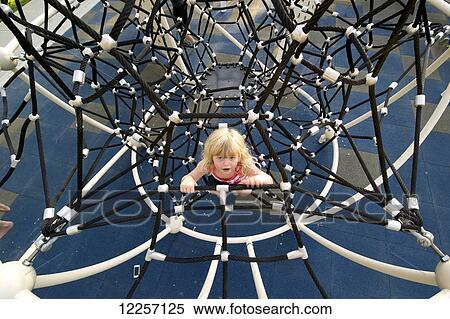 Stock Photography - Young girl climbing on playground equipment; Lethbridge, Alberta, Canada. Fotosearch