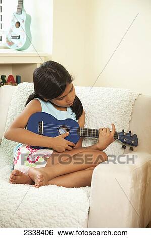 Stock Photograph - Young Girl Curled Up And Playing A Ukulele; San Francisco, California, Usa. Fotosearch