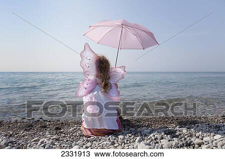 Stock Image - Young Girl Holding A Pink Parasol And Wearing Fairy Wings On The Shore Of Lake Ontario; Whitby Ontario Canada. Fotosearch