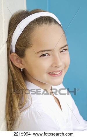 Young girl in front of a blue wall, wearing a white shirt and headband. View Large Photo Image Picture - Young girl in front of a blue wall, wearing a white shirt and headband.. Fotosearch