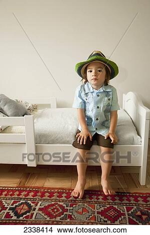 Picture - Young Girl In Hat Sitting On Her Bed; San Francisco, California, Usa. Fotosearch