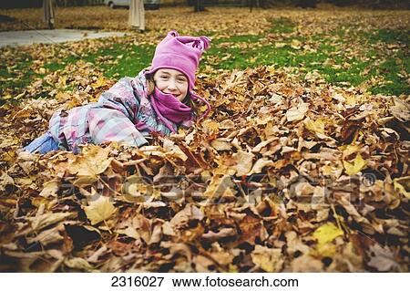 Stock Photo - Young Girl In Pink Hat And Scarf Lying In A Pile Of Autumn Leaves; Maricourt Quebec Canada. Fotosearch