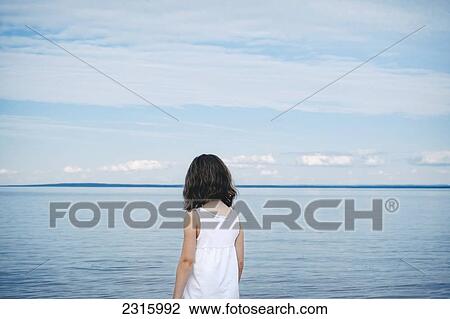 Stock Image - Young Girl In White Top Facing A River; Saint-Simeon Quebec Canada. Fotosearch