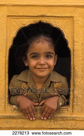 Stock Image - Young girl in window of ochre building, Jaisalmer, Rajasthan, India. Fotosearch