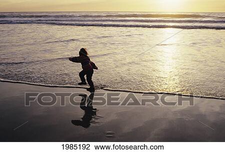 Stock Image - Young Girl Playing Along Oceanside, Silhouetted At Sunset.. Fotosearch