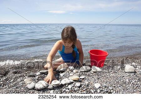 Young girl playing on a pebble beach on the shore of lake ontario; Ontario canada View Large Photo Image Picture - Young girl playing on a pebble beach on the shore of lake ontario; Ontario canada. Fotosearch