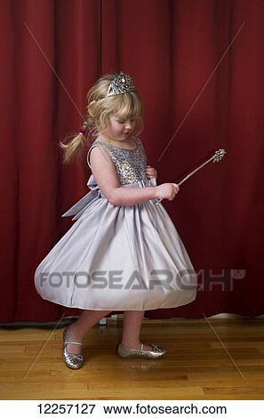Stock Photo - Young girl poses in front of a red curtain dressed in a silver dress with a wand; Millet, Alberta, Canada. Fotosearch