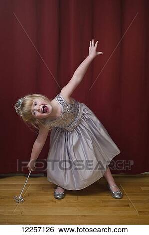 Stock Photograph - Young girl poses in front of a red curtain dressed in a silver dress with a wand; Millet, Alberta, Canada. Fotosearch