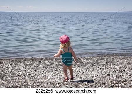 Stock Photograph - Young girl running on a pebble beach by the shore of lake ontario; Ontario canada. Fotosearch