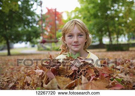 Stock Image - Young girl sitting in pile of leaves in autumn; Picton, Ontario, Canada. Fotosearch