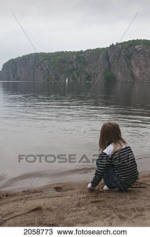 Stock Image - Young Girl Sitting On The Edge Of Mazinaw Lake, Looking At Bon Echo Rock, Bon Echo Provincial Park, Ontario, Canada. Fotosearch