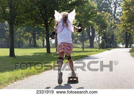 Stock Photo - Young Girl Skateboarding While Wearing Fairy Wings; Whitby Ontario Canada. Fotosearch