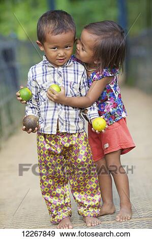 Stock Photo - Young girl whispering to a young boy; Battambang, Cambodia. Fotosearch