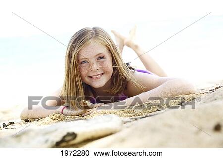 Stock Image - Young Girl With Red Hair And Freckles Laying In Sand On Beach. Fotosearch