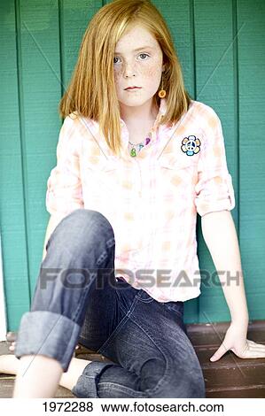 Stock Photo - Young Girl With Red Hair And Freckles Sits On A Porch Against A Blue Wall.. Fotosearch