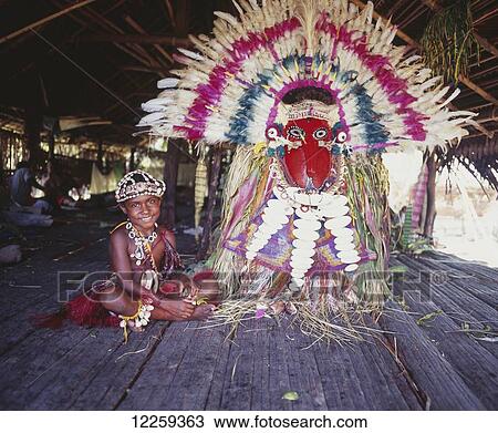 Stock Image - Young girl with Sepik river ceremonial headress in the background; East Sepik, Papua New Guinea. Fotosearch