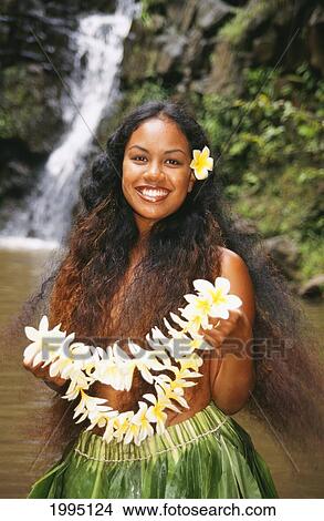 Picture - Young Hawaiian Woman In Ti-Leaf Skirt Stands Before A Waterfall Holding Plumeria Lei.. Fotosearch