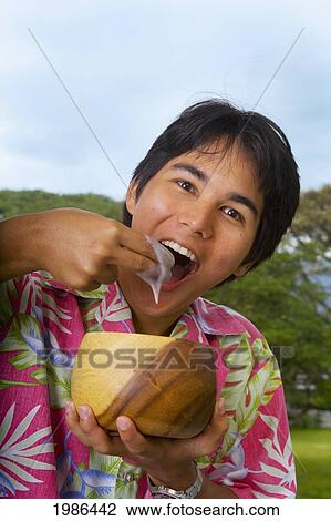 Stock Image - Young Man Eating Poi With Fingers Out Of Wooden Bowl.. Fotosearch