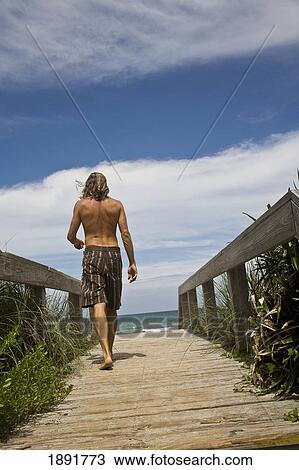 Stock Image - Young Man Walking On Wooden Deck Towards Melbourne Beach. Fotosearch