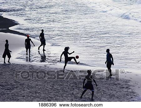 Stock Photograph - Young Men Playing Football On The Beach. Fotosearch