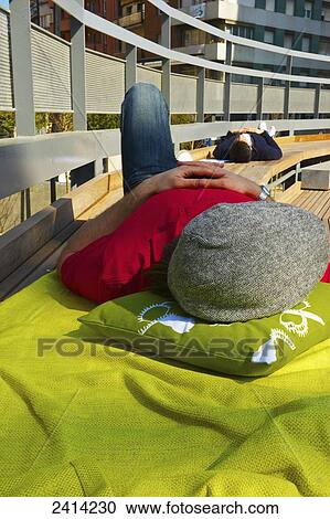 Stock Image - Young men snoozing on a bench in an urban area; Barcelona, Spain. Fotosearch
