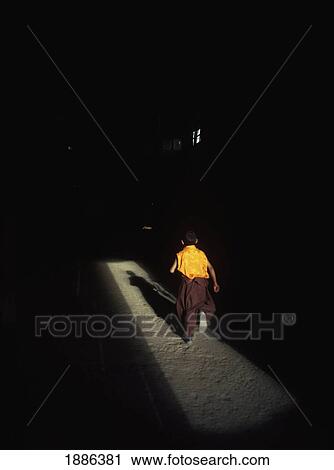 Stock Image - Young Monk Running Into Prayer Hall Of Tsemo Monastery. Fotosearch
