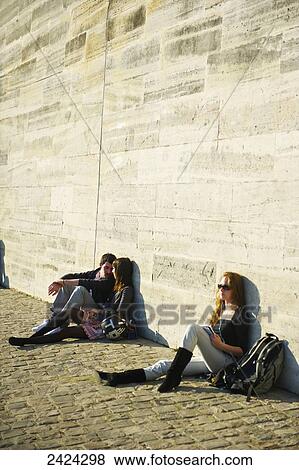 Stock Photo - Young people sitting against a wall in the sun; Paris, France. Fotosearch