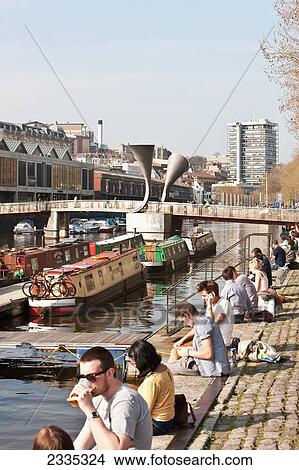 Picture - Young People Sitting At Edge Of Waterfront With Pero's Bridge In Background, Harborside; Bristol, England, Uk. Fotosearch