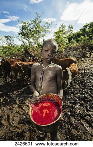 Stock Image - Young Suri (Surma) tribe cattle herder with bowl of blood taken from cow, Omo region, Southwest Ethiopia; Kibish, Ethiopia. Fotosearch